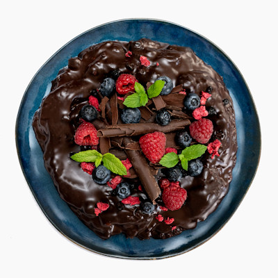 Čokodort Lesní Plody bohatě ozdobený čokoládovými hoblinami a lyofilizovaným ovocem na modrém talíři